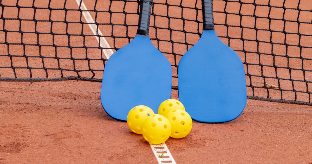 Two pickleball paddles and three balls resting on a court