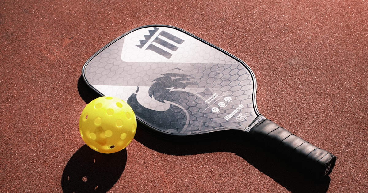 A pickleball paddle and ball on a court surface
