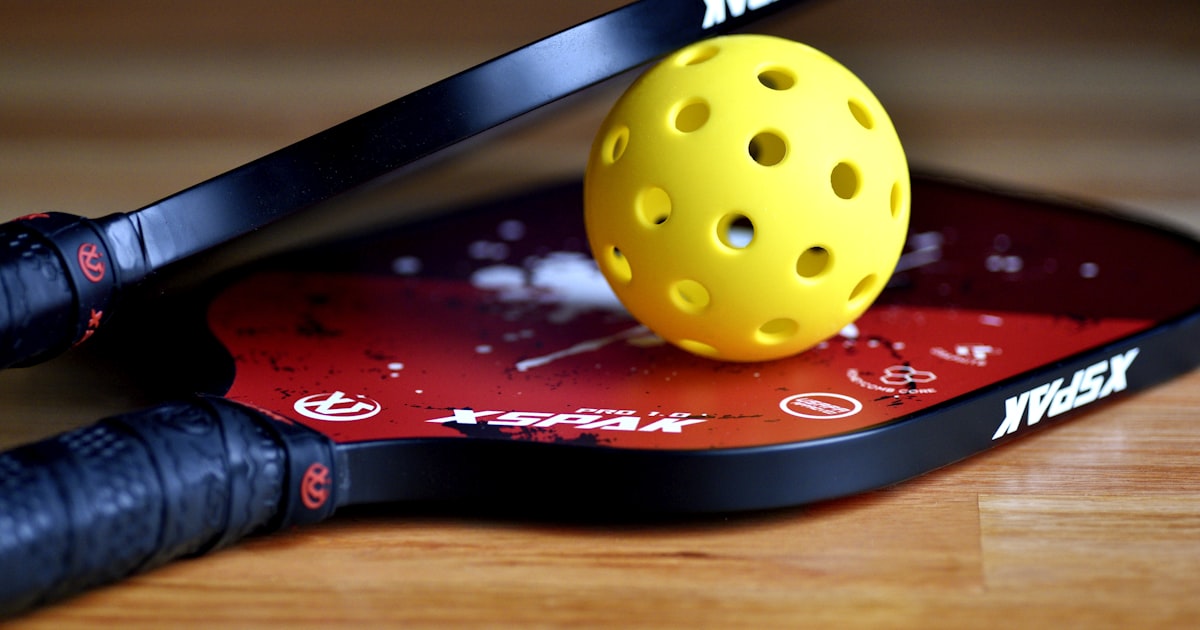 A yellow pickleball ball resting on top of a paddle face