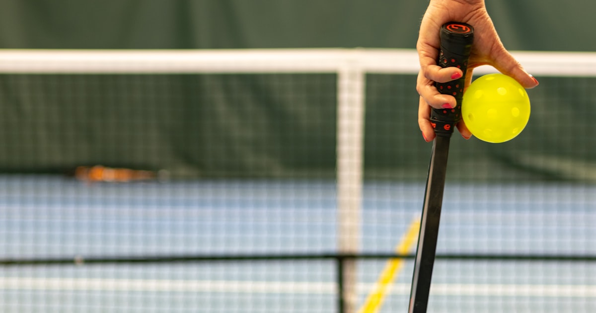 A player holding a pickleball ball and paddle, ready to serve