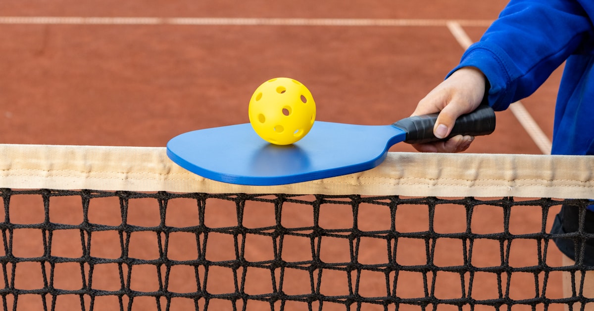 A player holding a pickleball paddle and ball on a court